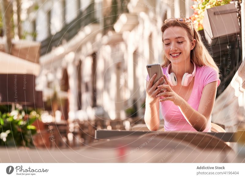 Lächelnde Teenagerin, die auf der Straße sitzend mit ihrem Smartphone Nachrichten austauscht Frau benutzend Surfen Texten Anschluss positiv zuschauen blättern