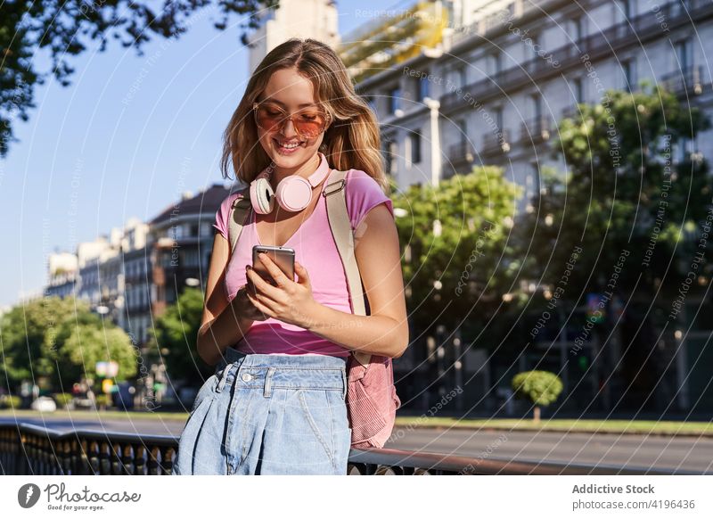 Lächelnde Teenagerin, die ein Smartphone benutzt und sich an ein Geländer auf der Straße lehnt Frau Browsen benutzend genießen Texten positiv zuschauen