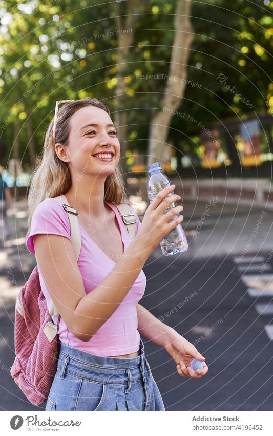 Lächelnde Teenagerin mit Wasserflasche im Park Frau Tourist Flasche Feiertag froh Urlaub Reise Rucksack sonnig Optimist stehen Lifestyle trinken Freude