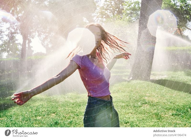 Glückliche Teenager-Frau unter Gischt im Park stehend positiv Sonnenschein genießen Freude sorgenfrei platschen expressiv Natur Lächeln heiter Optimist sonnig