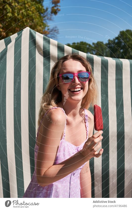 Lachende Teenager-Frau, die an einem sonnigen Tag Eis isst Stieleis süß Freude sorgenfrei expressiv Glück Optimist Sonne genießen Sommer Kleid positiv Glee froh