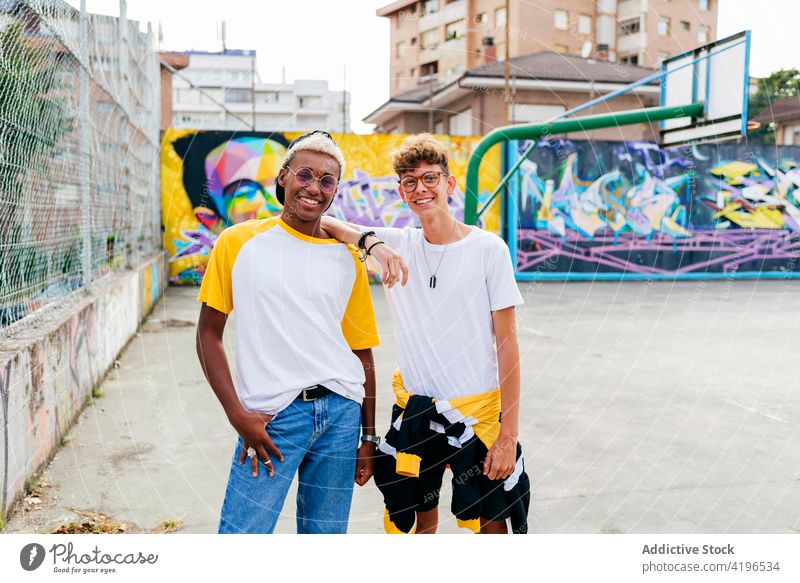 Zwei Teenager stehen und lachen auf dem städtischen Basketballplatz Herbst schwarz Junge Kaukasier heiter Großstadt farbenfroh Gesellschaft Tageslicht ethnisch