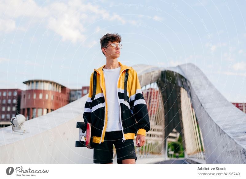 Kaukasischer Teenager mit Skateboard auf der Brücke in der Stadt stehend Herbst blond Junge Kaukasier Großstadt farbenfroh selbstbewusst Tageslicht Freizeit