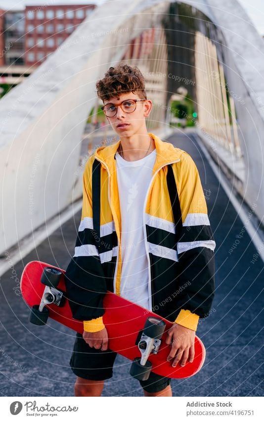 Kaukasischer Teenager mit Skateboard auf der Brücke in der Stadt stehend blond Junge Kaukasier Großstadt farbenfroh selbstbewusst Freizeit männlich Mann Model