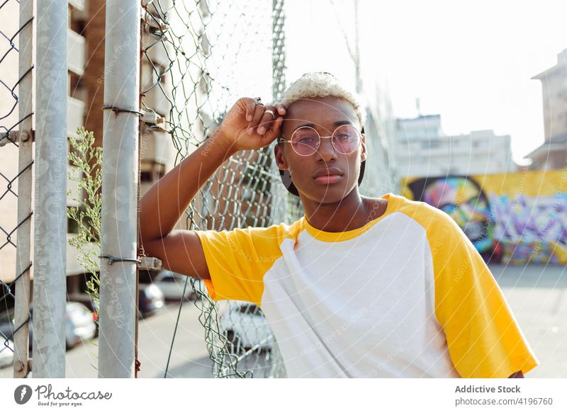 Hübscher junger schwarzer Mann liegt auf einem Zaun auf der Straße attraktiv Junge Verschlussdeckel heiter Großstadt farbenfroh selbstbewusst Tageslicht
