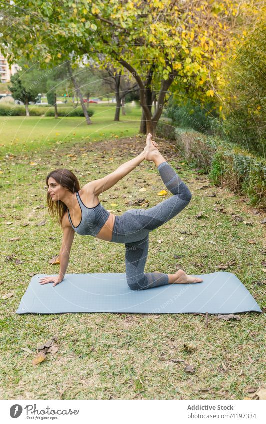 Schlanke Frau beim Yoga in Halbmond-Lunge-auf-dem-Knie-Haltung beweglich üben Asana Harmonie Park Unterlage Dehnung Gesundheit Sportbekleidung friedlich