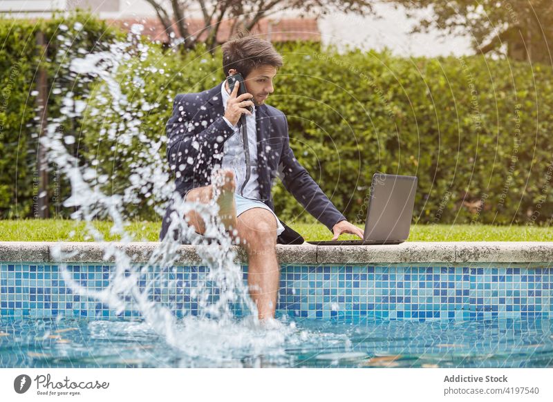 Geschäftsmann im Anzug, der mit einem Laptop auf dem Beckenrand sitzt Arbeit Pool Person Schwimmsport Computer Business Mann Telefon sprechend Sprechen Internet