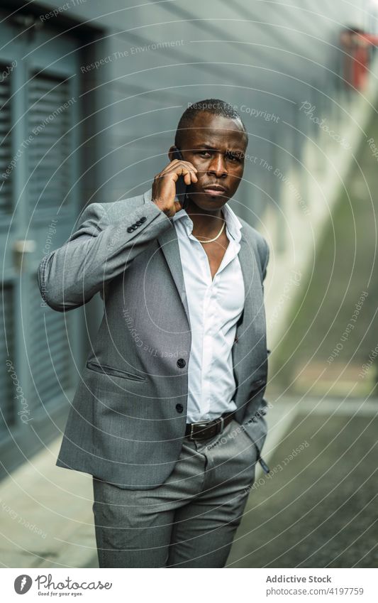 Seriöser schwarzer männlicher Chef spricht über Smartphone in der Stadt sprechen Afroamerikaner schwarzer Ernst Anzug maskulin Hand-in-Tasche Mann benutzend