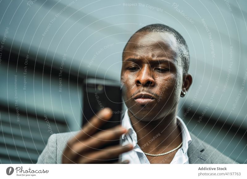 Seriöser schwarzer männlicher Chef, der in der Stadt ein Mobiltelefon durchsucht Smartphone Afroamerikaner schwarzer Ernst Anzug maskulin Mann benutzend Browsen