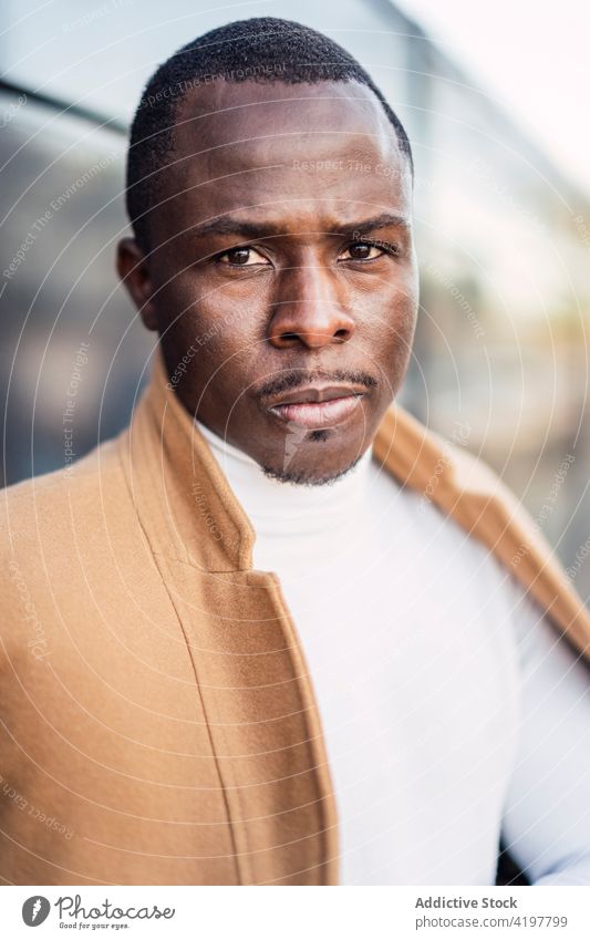 Ernster junger ethnischer Mann schaut auf der Straße in die Kamera ernst selbstbewusst Windstille Porträt Stil selbstsicher elegant Großstadt Persönlichkeit