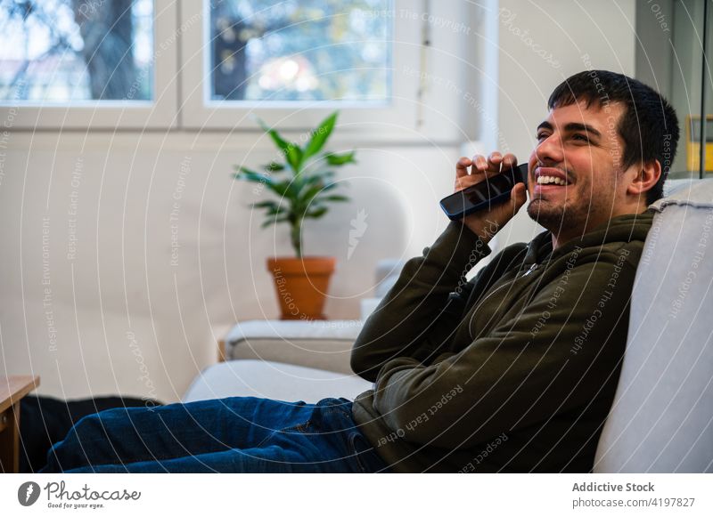Fröhlicher blinder Mann, der auf dem Sofa sitzend Audio hört benutzend zuhören Audiobotschaft Behinderung Smartphone positiv genießen Kommunizieren männlich