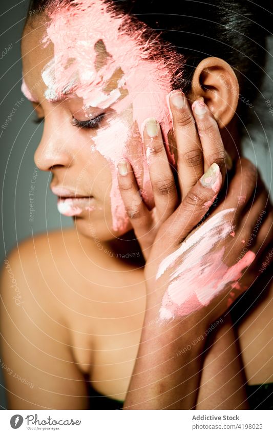 Ethnische Frau mit Farbe im Gesicht im Atelier Model kreativ Kunst exzentrisch Vorschein ethnisch Schliere Schmierfleck Kraulen Farbstoff Stil ungewöhnlich