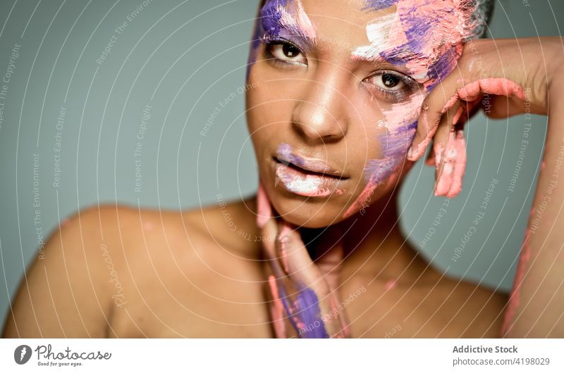 Ethnische Frau mit Farbe im Gesicht im Atelier Model kreativ Kunst exzentrisch Vorschein ethnisch Schliere Schmierfleck Kraulen Farbstoff Stil ungewöhnlich