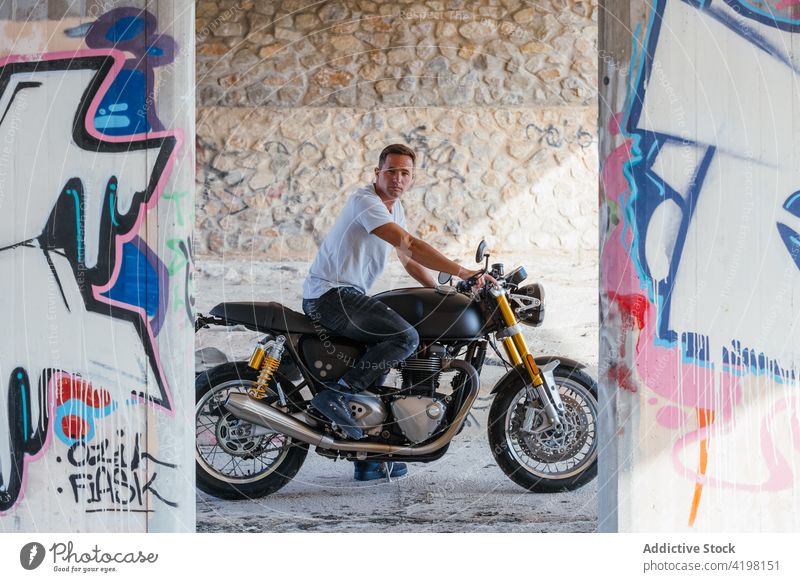 Mann auf modernem Motorrad in der Stadt Biker cool urban Stil Motorradfahrer Fahrzeug selbstbewusst männlich sitzen brutal Graffiti Wand Straßenkunst Verkehr