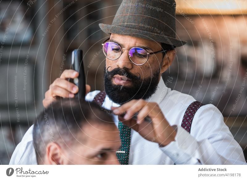 Ethnischer Friseur schneidet die Haare eines Kunden mit einem Trimmer im Friseursalon entgittern Behaarung Klient Schermaschine Verfahren Schönheit Macho