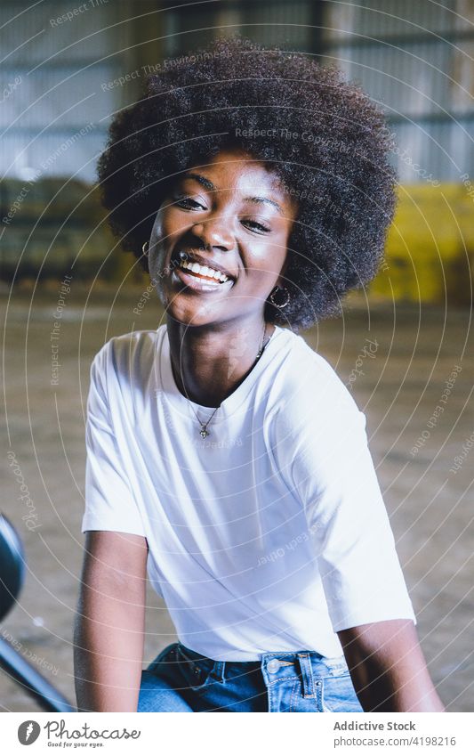 Selbstbewusste junge schwarze Frau, die lächelnd im Hangar sitzt Lächeln heiter ruhen selbstbewusst Glück industriell Stil Freude positiv froh modern
