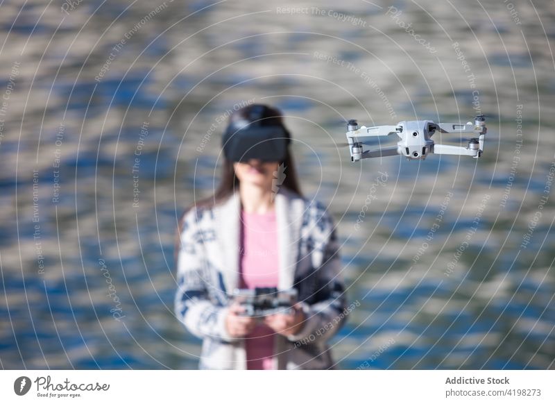 Fröhliche Frau mit VR-Brille steuert Drohne am Meer arbeiten Dröhnen virtuell Realität Flug abgelegen Kontrolle Fliege unbemannt Regler Gerät Apparatur