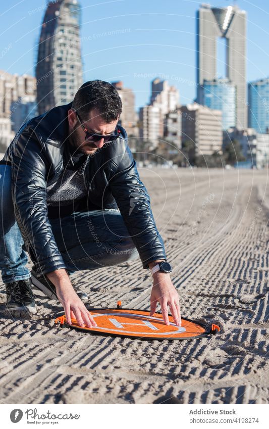 Mann legt Landematte für Drohne auf den Boden Dröhnen Landen Unterlage Sand behüten Hobby Sicherheit männlich Konzentration Fokus ernst sonnig vorbereiten