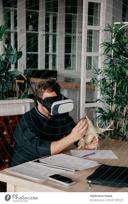 Anonymer Mann benutzt VR-Brille, während er in einem Restaurant mit Mais und Dokumenten sitzt Erfahrung Arbeit Schriftstück Virtuelle Realität digital
