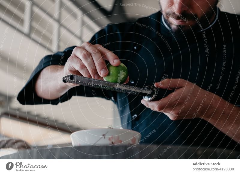 Anonymer männlicher Koch, der beim Kochen im Restaurant eine Zutat zum Essen hinzufügt Mann Küchenchef Reibeisen reiben Schale Prozess hinzufügen Bestandteil