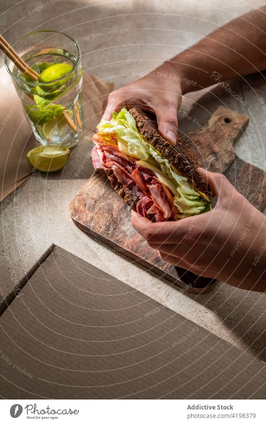 Crop-Person beim Mittagessen mit Sandwich und einem Glas Wasser Klient Belegtes Brot Zuprosten Salat Speck Restaurant geschmackvoll Kalk frisch Café Schinken