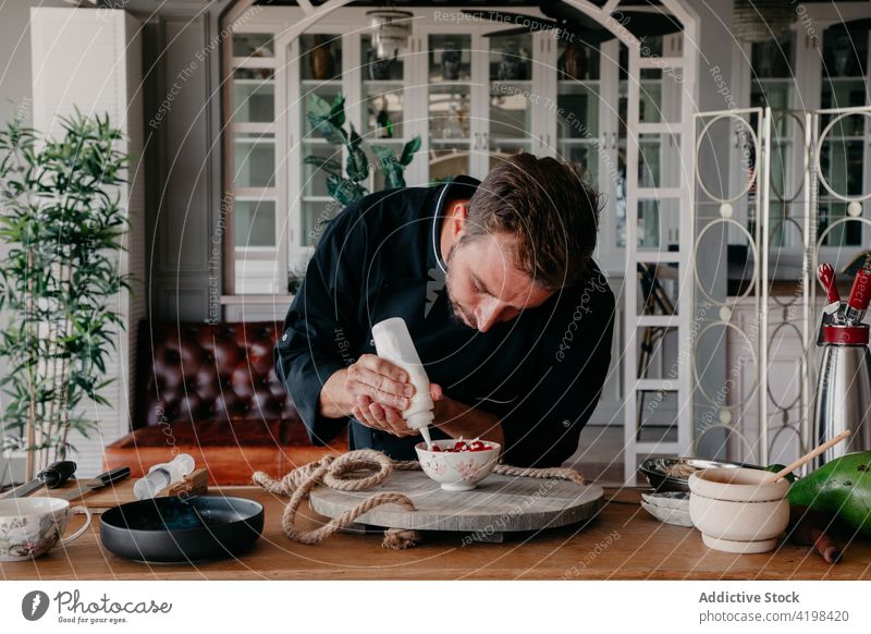 Konzentrierter Mann dekoriert Dessert mit Sahne in einem stilvollen Restaurant dekorieren Küchenchef Beeren lecker Koch Konzentration Job kulinarisch