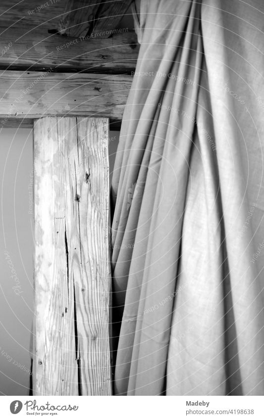 Altes Gebälk aus Holz mit Vorhang aus Stoff in der restaurierten Dachwohnung eines alten Bauernhaus in Rudersau bei Rottenbuch im Kreis Weilheim-Schongau in Oberbayern, fotografiert in klassischem Schwarzweiß