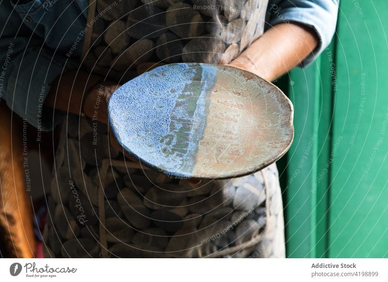 Gesichtsloser Töpfer zeigt eine Tonplatte in einem traditionellen Atelier Person manifestieren Teller Keramik Tonwaren Kunstgewerbler handgefertigt Handwerk