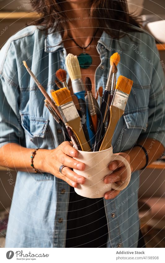 Anonyme Handwerkerin hält Tasse mit verschiedenen Pinseln in einer Werkstatt Frau Pinselblume Meister Töpferwaren Tonwaren heiter Kunstgewerbler Bürste Werkzeug