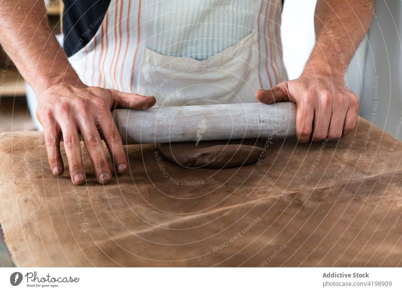 Anonymer Mann knetet Ton, während er in einer Werkstatt Geschirr herstellt hochkrempeln Tonwaren kreieren Nudelholz Job Basteln Töpferwaren Arbeit Handwerk