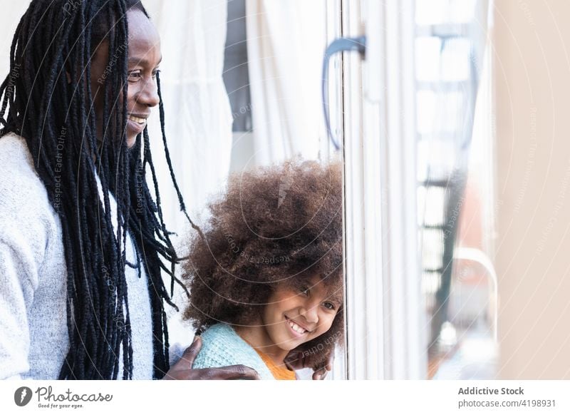 Schwarzer Vater mit Tochter steht am Fenster schließen heiter sorgenfrei Bonden positiv Angebot Lächeln Umarmung Mädchen Mann Papa Kindheit Afro-Look Eltern