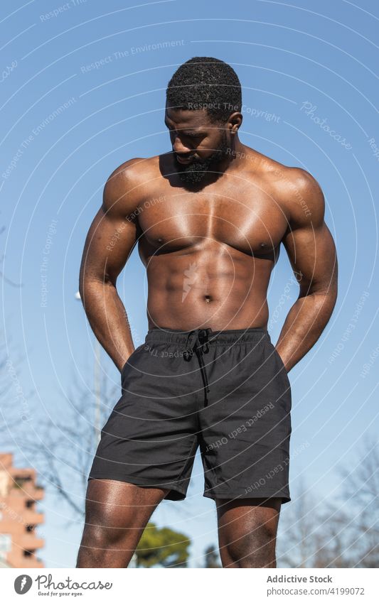 Starker ethnischer Sportler ruht sich beim Training auf dem Sportplatz aus nackter Torso stark ruhen muskulös Wellness Hand an der Hüfte Mann ohne Hemd