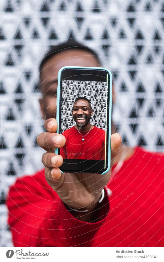 Schwarzer Mann zeigt Foto auf Smartphone-Bildschirm heiter herzlich Deckblatt Macho freundlich benutzend Apparatur zeigen Gerät maskulin hell Afroamerikaner