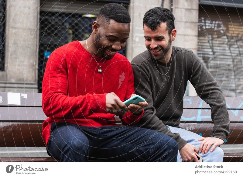Fröhliche Menschen mit Smartphone auf einer Bank in der Stadt Freund Glück Straße Männer benutzend Apparatur Gerät Macho maskulin lässig anhaben Zusammensein