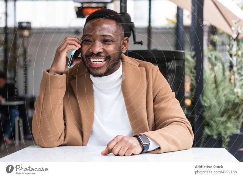 Zufriedener schwarzer Mann, der in einem Café mit seinem Smartphone spricht sprechen Glück Mode maskulin gut gekleidet genießen Tisch benutzend Apparatur Gerät
