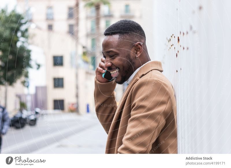Gut gekleideter glücklicher schwarzer Mann telefoniert mit seinem Smartphone an der Wand sprechen Internet maskulin heiter Telefonanruf Macho benutzend