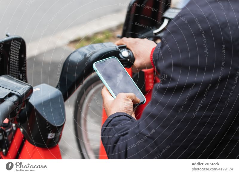 Anonymer ethnischer Mann nutzt Smartphone-App zum Fahrradparken zuschauend maskulin Macho Stadt benutzend Apparatur Gerät Verkehr hell Internet online