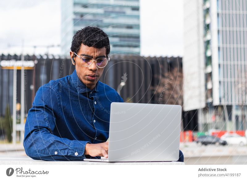 Seriöser ethnischer männlicher Freiberufler arbeitet am Laptop in der Stadt Mitarbeiter freiberuflich Arbeit Ohrstöpsel zuhören nachdenklich Mann benutzend