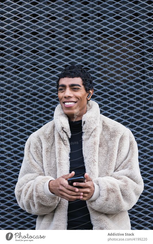 Inhalt stilvoller ethnischer Mann mit Smartphone im Ohrhörer auf der Straße Ohrstöpsel zuhören Gesang genießen trendy Drahtlos benutzend Apparatur Gerät Glück