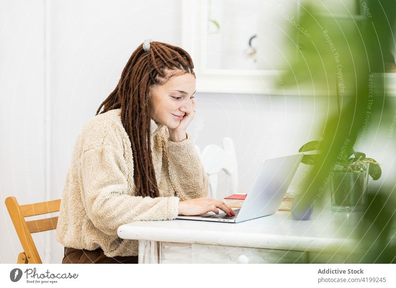 Nachdenkliche Frau mit Dreadlocks, die zu Hause mit einem Laptop arbeitet heimwärts Computer Sitzen Raum Internet Technik & Technologie Menschen Lifestyle jung