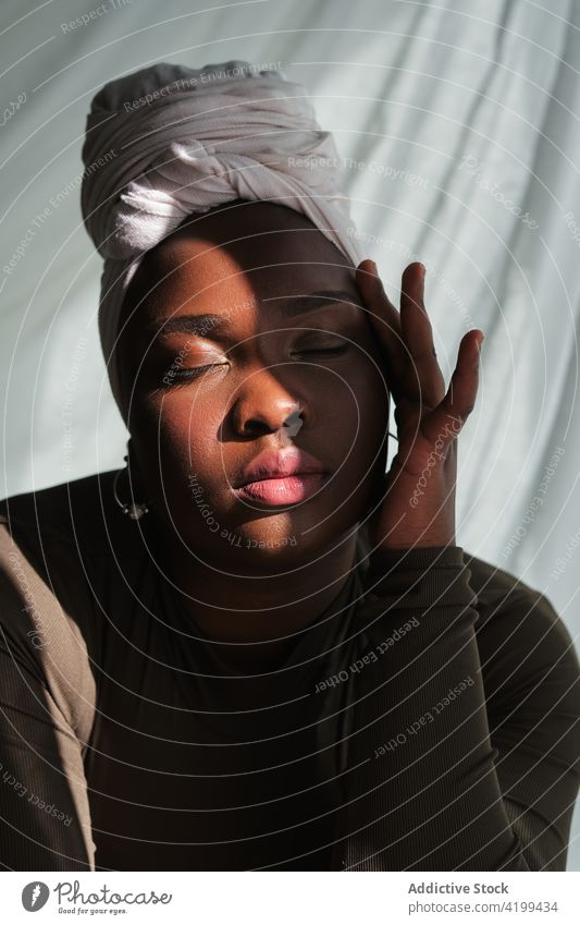 Junge schwarze Frau mit geschlossenen Augen, die ihr Gesicht berührt Augen geschlossen Gesicht berühren Anmut feminin sich[Akk] entspannen Tradition Stil
