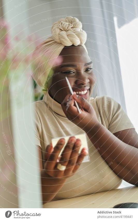 Fokussierte stilvolle schwarze Frau, die zu Hause Eyeliner aufträgt bewerben Kajal Make-up Spiegel Schönheit Routine Kosmetik Stil Menschliches Gesicht
