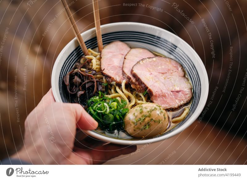 Mann mit einer Schüssel Ramen-Suppe Essstäbchen Restaurant Speise essen Asiatische Küche Schinken geschmackvoll männlich Lebensmittel Mahlzeit schmackhaft