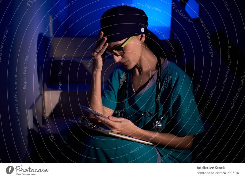 Arzt benutzt Smartphone in dunkler Klinik benutzend lesen Schriftstück Zwischenablage nachdenklich Browsen Frau Sanitäter untersuchen medizinisch Bericht