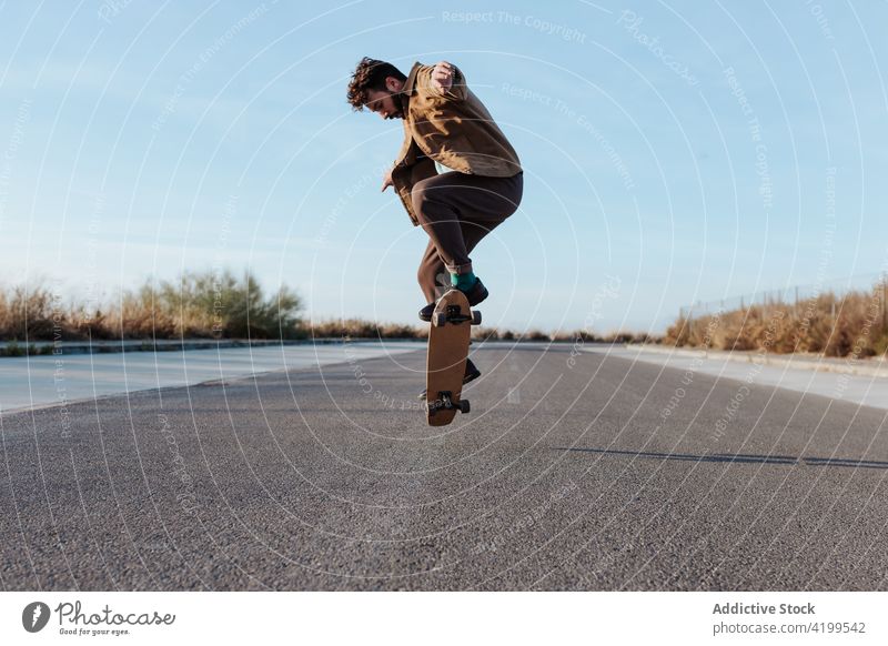 Energetischer junger Skater, der einen Trick auf dem Skateboard vorführt Mann Kickflip springen Stunt Energie Fähigkeit Straße Landschaft Natur ländlich