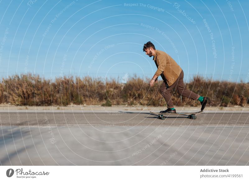 Junger bärtiger Skater auf Asphaltstraße Mann Mitfahrgelegenheit Straße Skateboard Landschaft ländlich Natur Hobby Subkultur üben Fähigkeit männlich Energie
