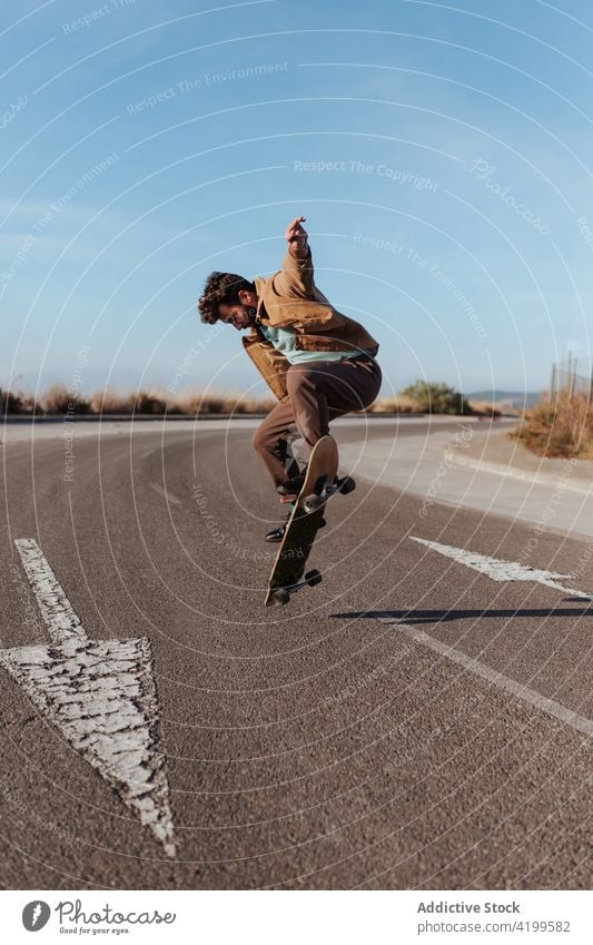 Energetischer junger Skater, der einen Trick auf dem Skateboard vorführt Mann Kickflip springen Stunt Energie Fähigkeit Straße Landschaft Natur ländlich