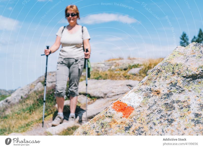 Aktive Frau, die mit Stöcken auf einem steinigen Berghang spazieren geht Spaziergang Stangengehen aktiv Hügel Weg Energie Trekking Nordic Walking physisch Mark