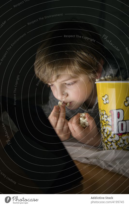 Kind auf der Couch, das auf dem Tablet fernsieht und Popcorn isst Junge genießen Filmmaterial Tablette Liege Spaß haben Cartoons Lifestyle Sofa Kinder Snack