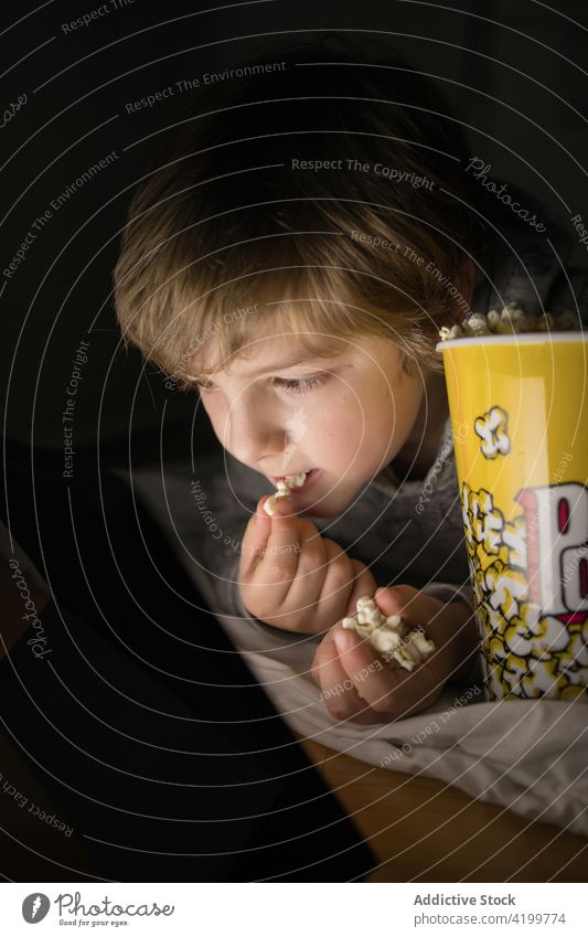 Kind auf der Couch, das auf dem Tablet fernsieht und Popcorn isst Junge genießen Filmmaterial Tablette Liege Spaß haben Cartoons Lifestyle Sofa Kinder Snack